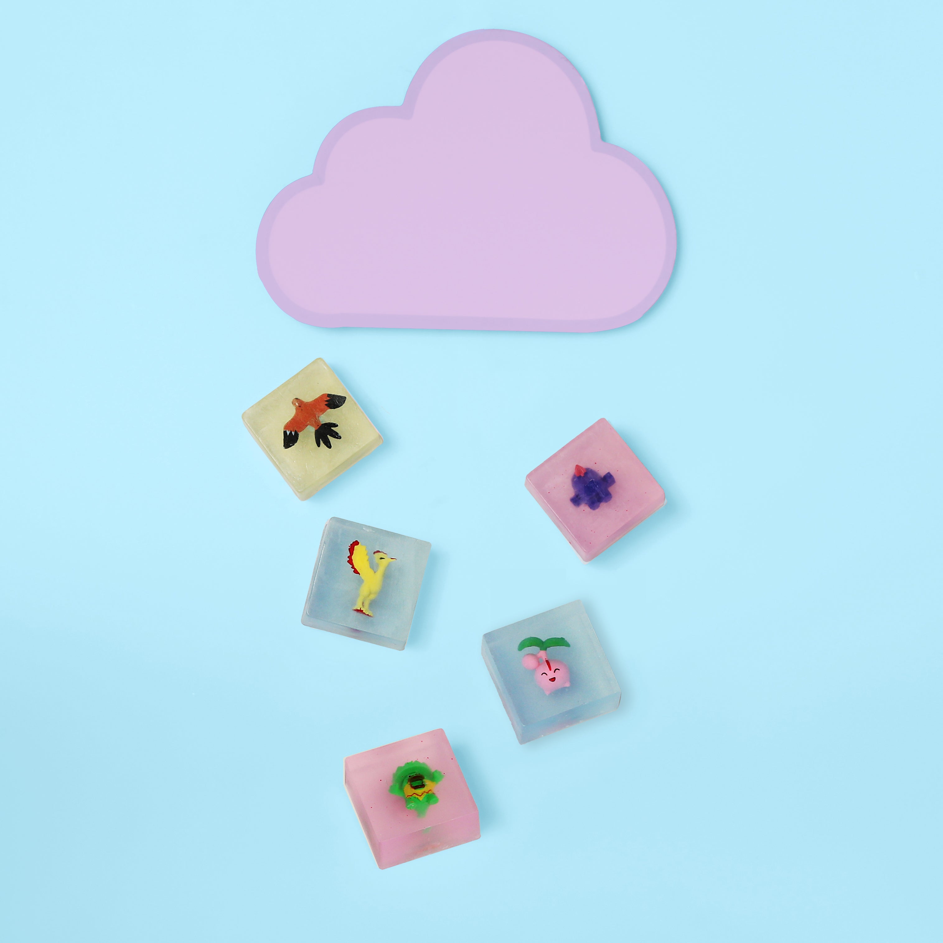 Blue background with pink cloud and a collection of five soaps beneath it. Clear glycerin like soap with toy inside.