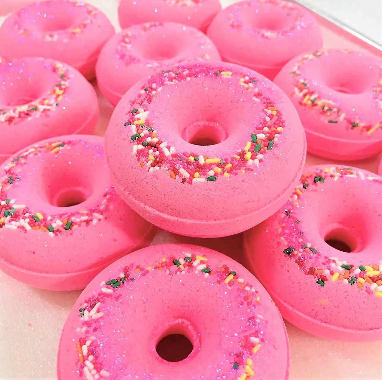 Hot pink donut shaped bath baths laid onto a tray. Bath bombs have a sprinkle and glitter top.