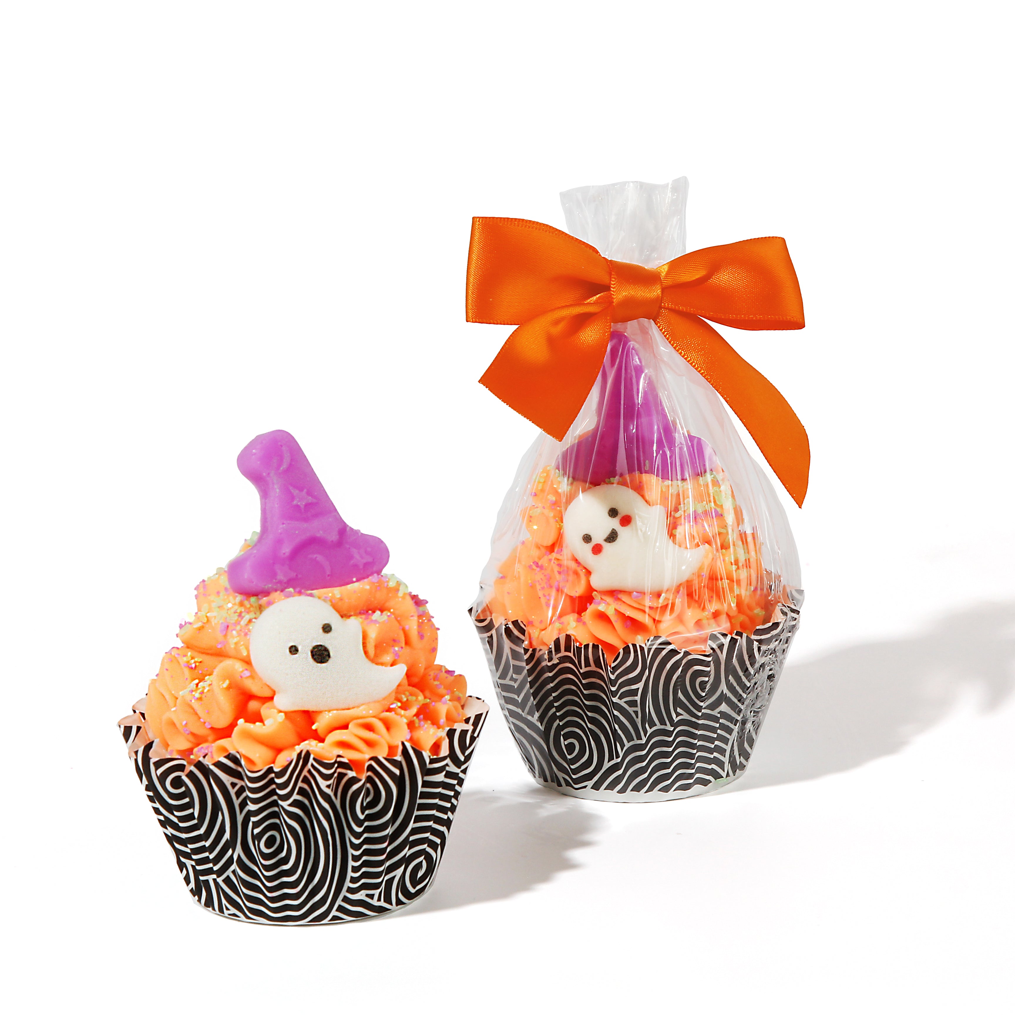 Realistic sized soap cupcake with a and black and white spiral patterned line. Bright orange soap frosting with a small ghost decoration and purple witch hat topper. Next to it is the same cupcake but packaged in a clear bag and tied with an orange bow.