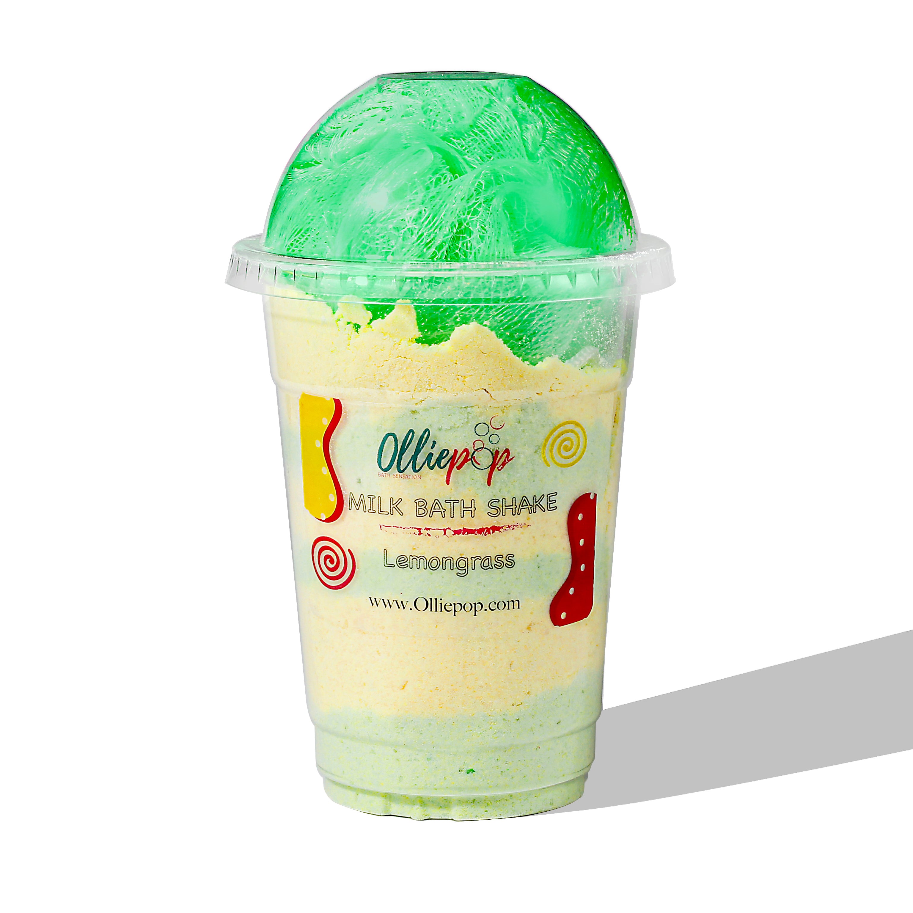 Plastic milkshake cup with light yellow milk bath soak inside. Green loofah on top with a dome lid.