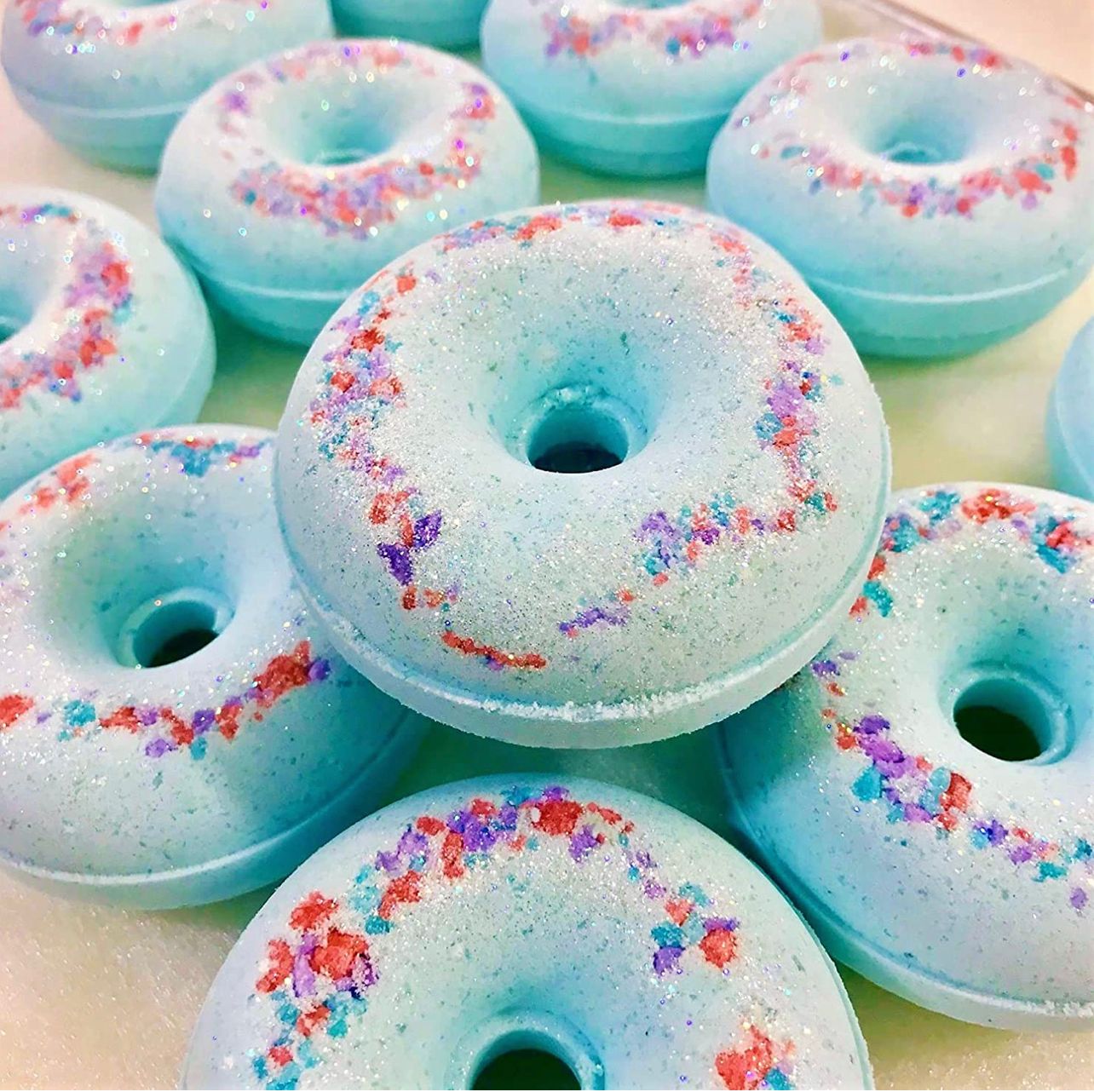 Our Cotton Candy bath bombs,  light blue with pastel confetti and glitter on the top. Several laid out in the picture and stacked neatly.